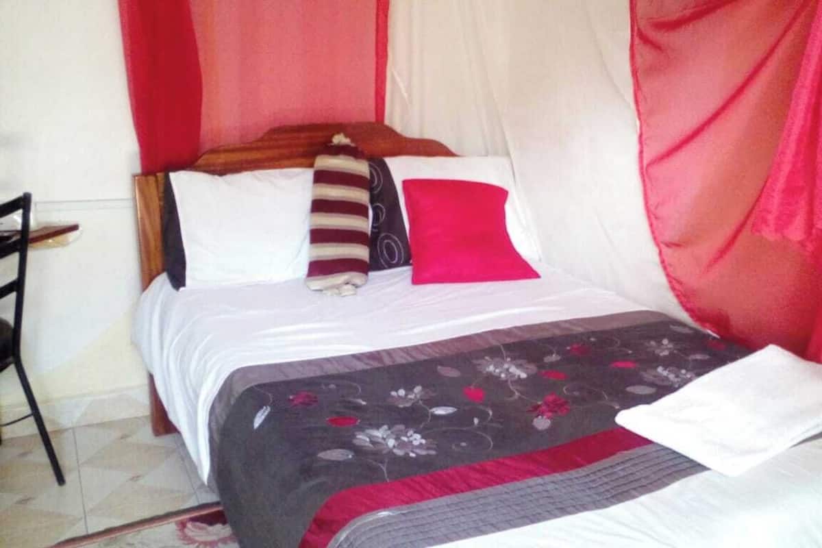 A bed with a floral bedspread, a wooden headboard, and a red pillow.