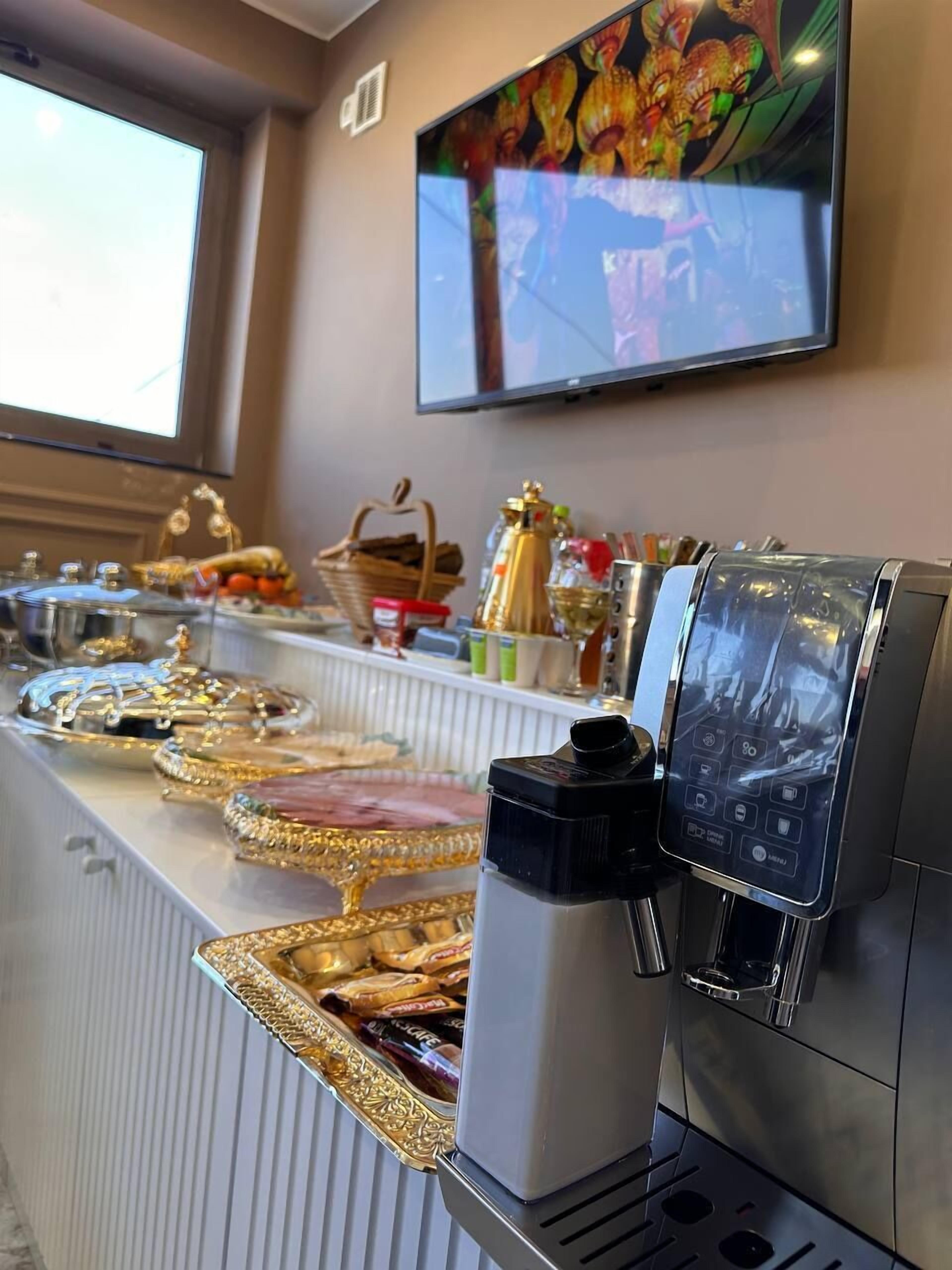 Zona de buffet con máquina de café, televisor montado en la pared y ventana que proporciona luz natural.
