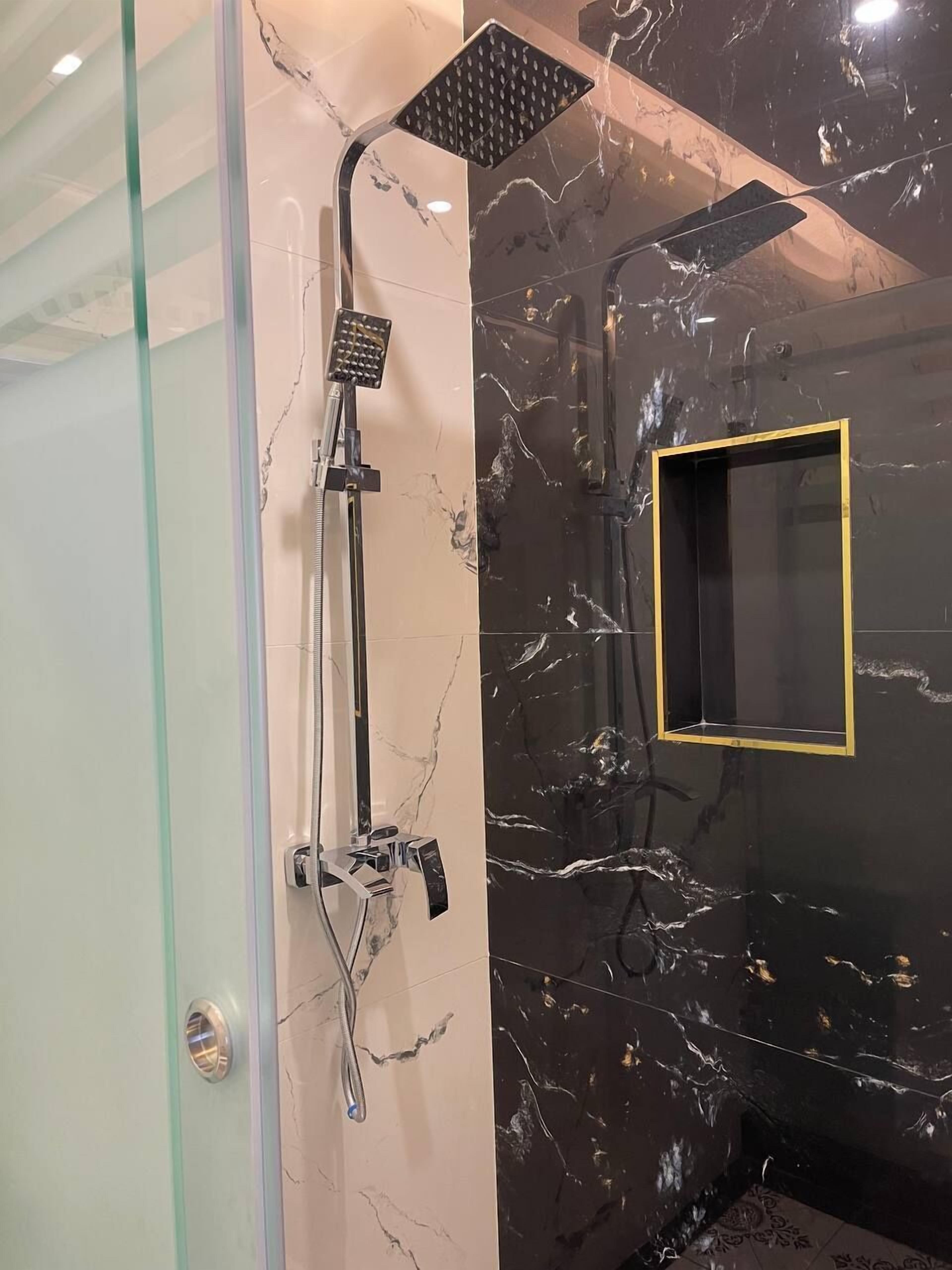 Un baño con cabina de ducha de vidrio, un cabezal de ducha de mano, un cabezal de ducha empotrado y una pared con azulejos de mármol.