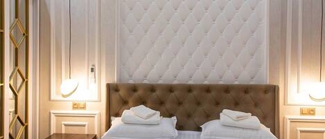 A hotel room with a tufted headboard, a bed with white linens, two bedside tables with lamps, and a mirror with a geometric frame.