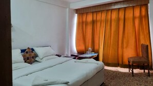 Habitación de hotel con una cama grande, una silla, una mesita de noche y una ventana con cortinas naranjas.