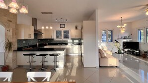A modern kitchen with a central island, bar stools, and a dining area with a wooden table. - Villa Francesca, Greek Garden Getaway in Agia Galini (Agia Galini)