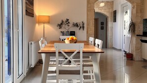 A modern dining area with a wooden table and white chairs, a stone wall, and a view through a glass door. - Villa Francesca, Greek Garden Getaway in Agia Galini (Agia Galini)