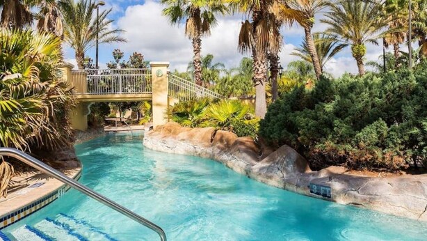 Una piscina cristalina con un puente, rodeada de vegetación tropical.