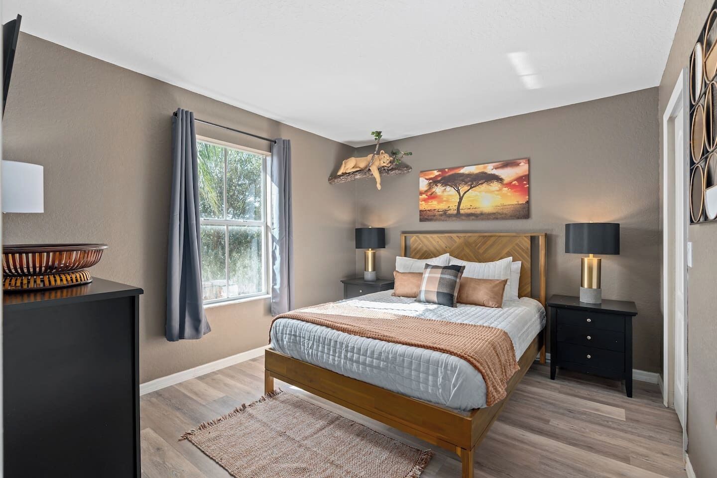 A bedroom with a bed, bedside tables, a window with curtains, a painting, and a lamp.