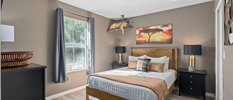 A bedroom with a bed, bedside tables, a window with curtains, a painting, and a lamp.
