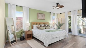 Un dormitorio con cama, mesita de noche, espejo, ventilador de techo y vistas a través de una puerta corrediza.