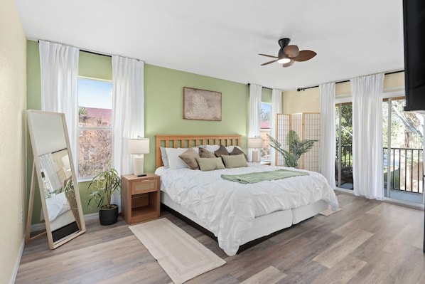A bedroom with a bed, a nightstand, a mirror, a ceiling fan, and a view through a sliding door.