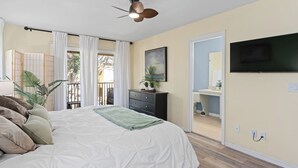 Un dormitorio con cama, cómoda, televisor, ventilador de techo y vista al exterior.