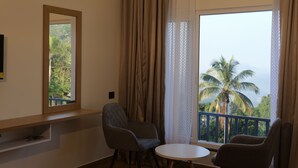 Ein Zimmer mit großem Fenster, einem Sessel, einem kleinen Tisch und einem Spiegel an der Wand.