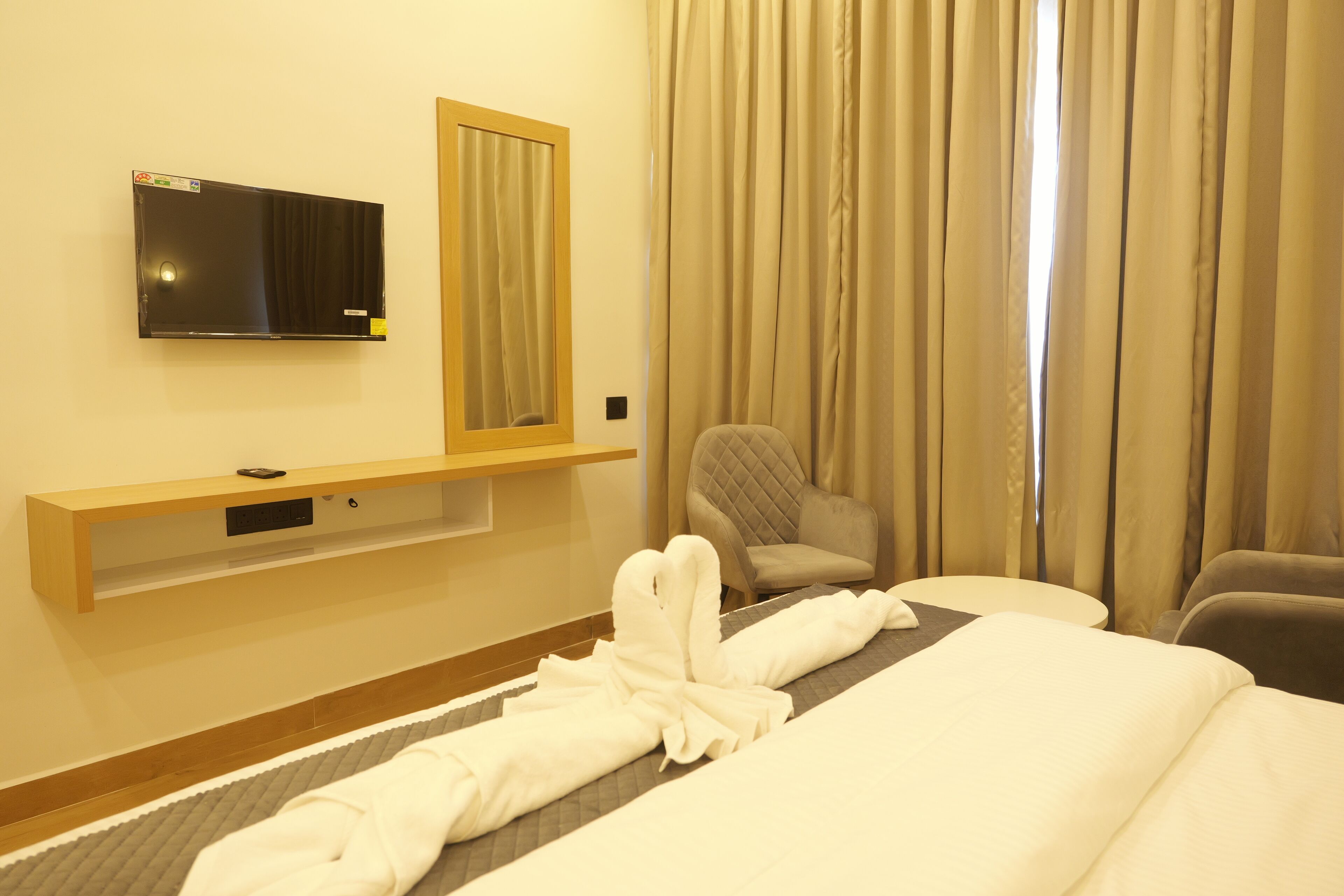 Ein Hotelzimmer mit Bett, Wandfernseher, Stuhl und einem fenster mit Vorhängen.