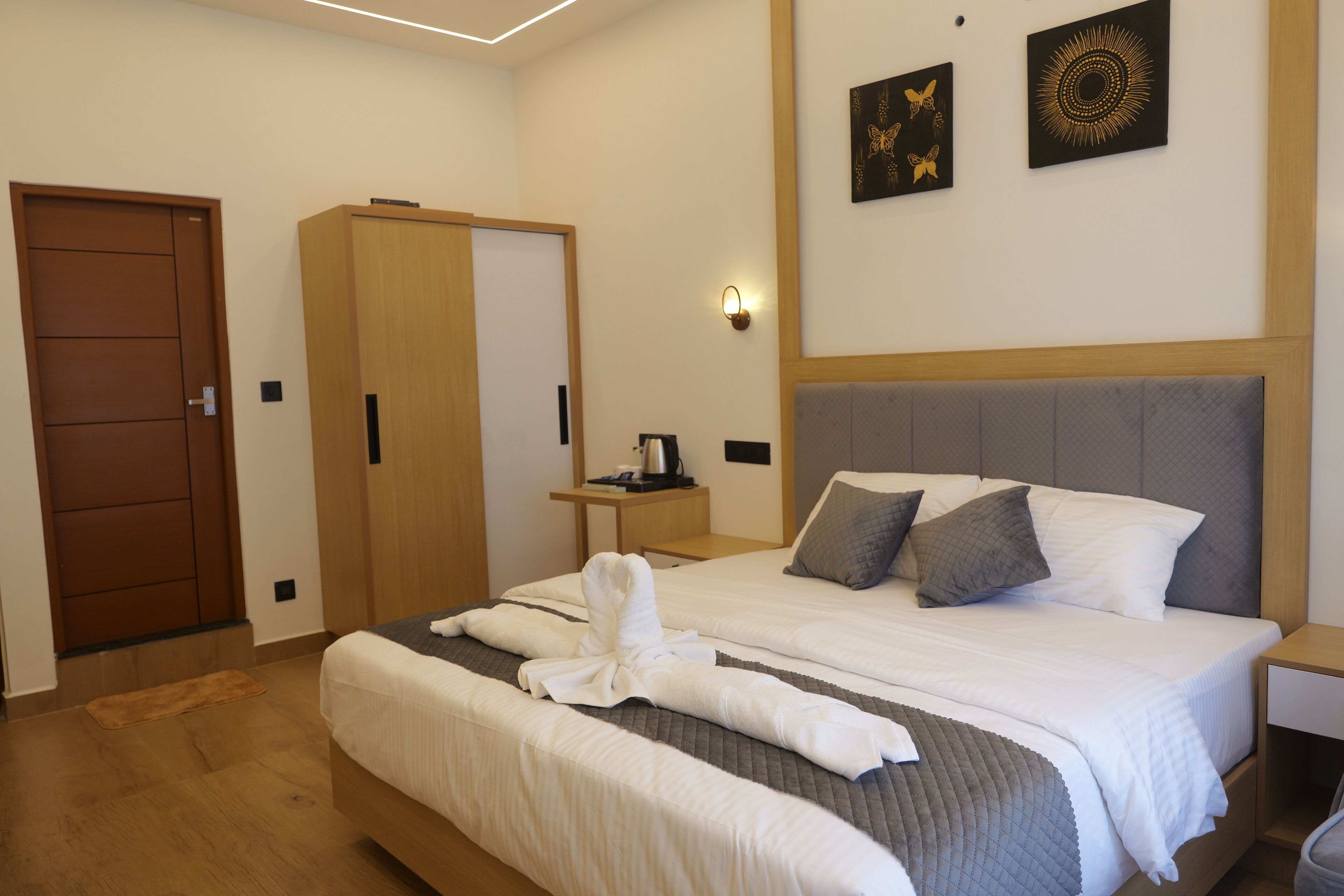 A hotel room with a large bed, a wardrobe, a bedside table with a lamp, and artwork on the wall.