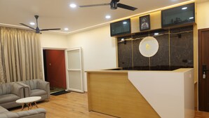 Ein modernes Wohnzimmer mit einer Couch, einem Couchtisch, einem hölzernen Empfangsschalter, einem Deckenventilator und einem an der Wand befestigten Fernseher.