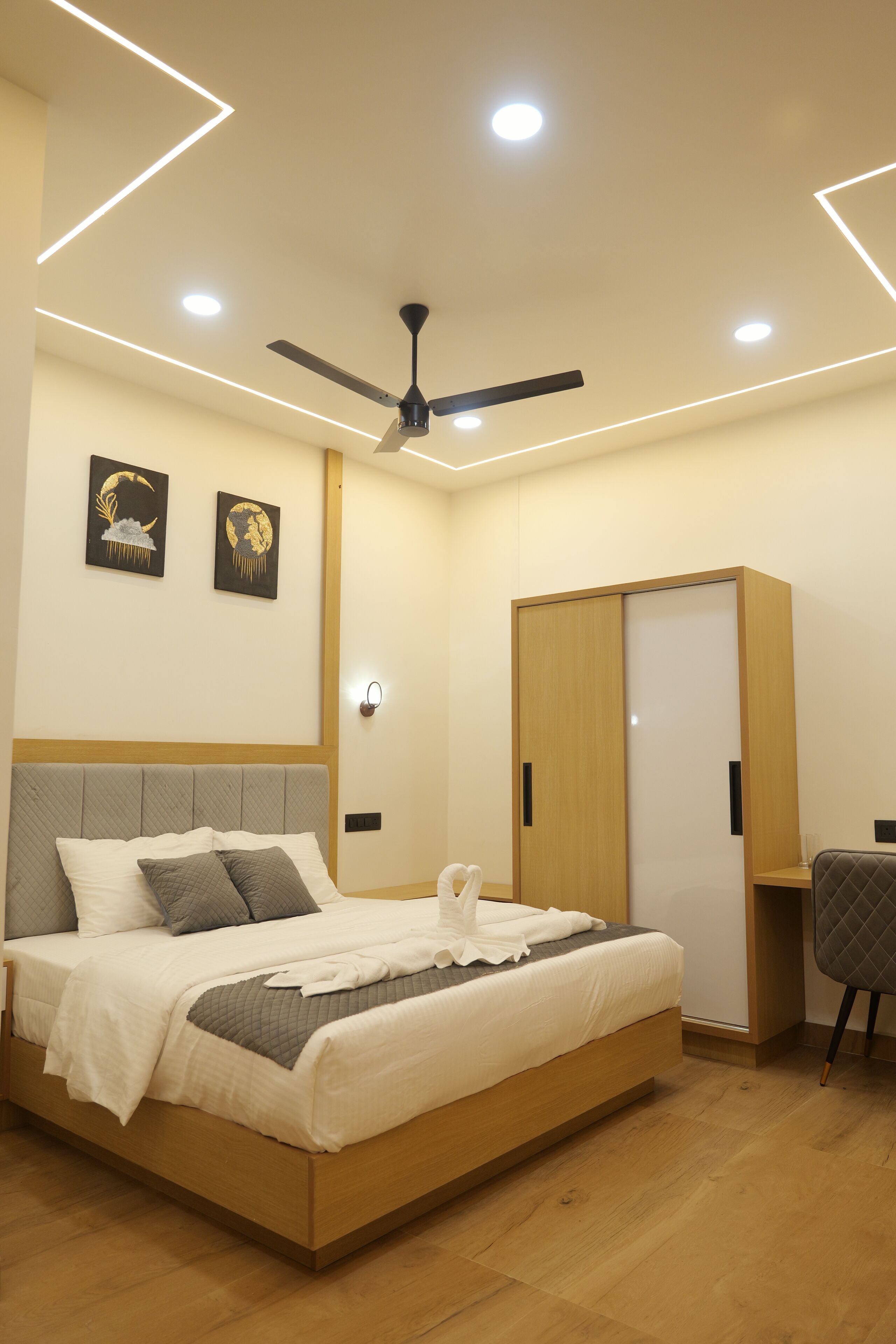 A modern bedroom with a bed, a ceiling fan, recessed lighting, a wardrobe, and artwork on the wall.