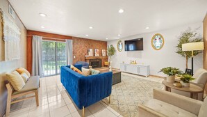 A modern living room with a blue sofa, a fireplace, a TV, and a large window. - 5 BR Jacuzzi 12 Mins to Disney Knotts Beach (Norwalk)