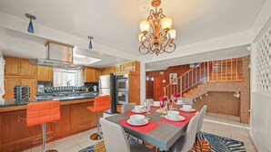 A modern kitchen with wooden cabinets, a stainless steel range hood, and a dining area with a table set for four. - 5 BR Jacuzzi 12 Mins to Disney Knotts Beach (Norwalk)