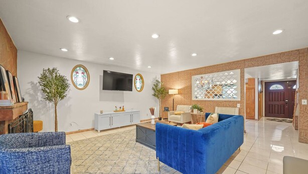 A modern living room with a blue sofa, a white armchair, and a TV mounted on the wall. There is a small cabinet and a plant in the corner. - 5 BR Jacuzzi 12 Mins to Disney Knotts Beach (Norwalk)