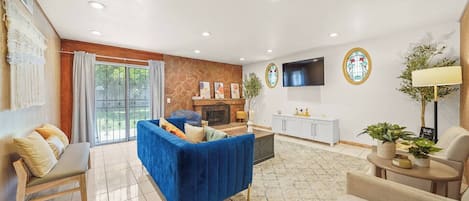 A modern living room with a blue sofa, a fireplace, a TV, and a dining area.
