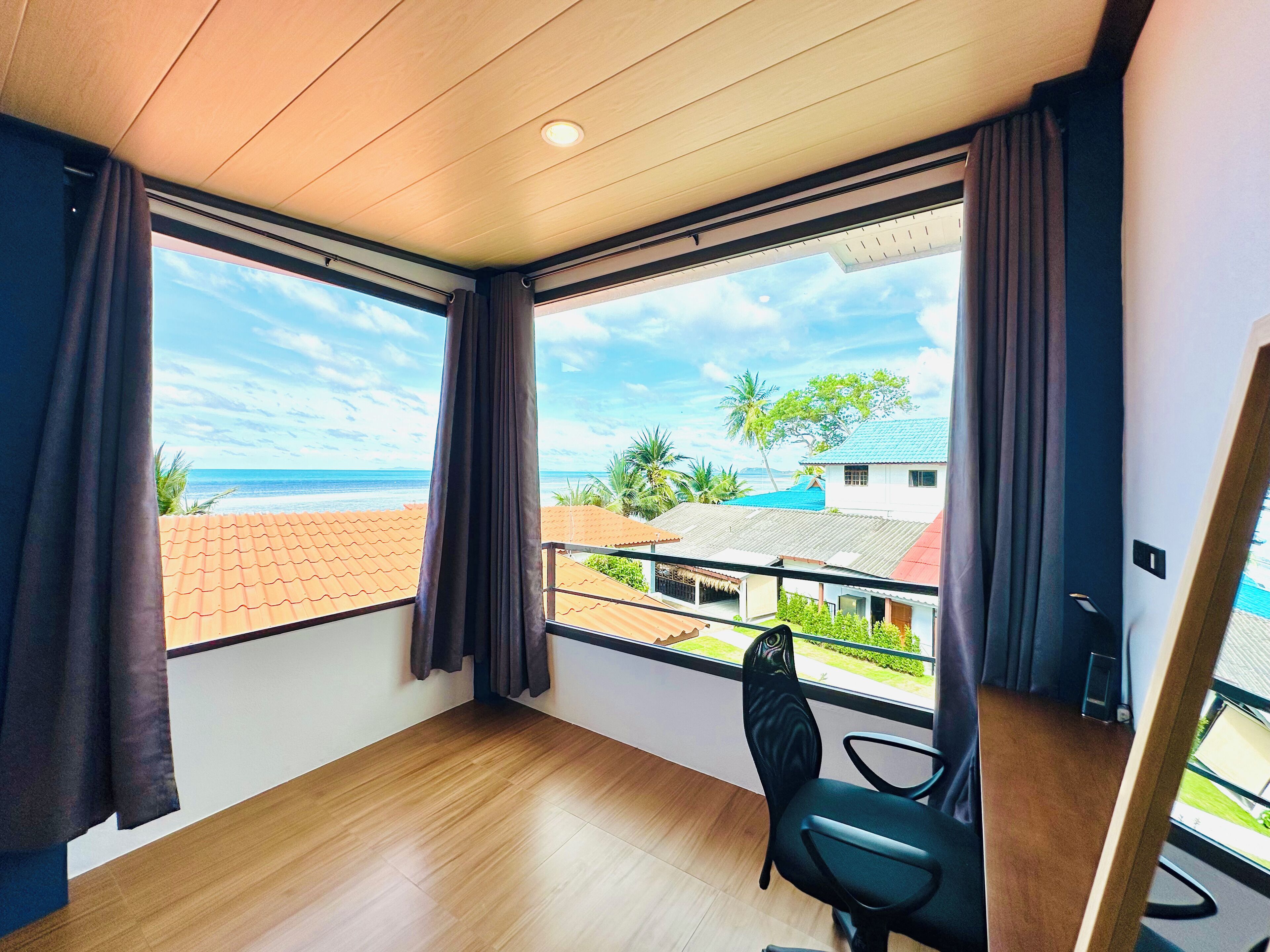 Una habitación con ventanas amplias, piso de madera y una silla negra.