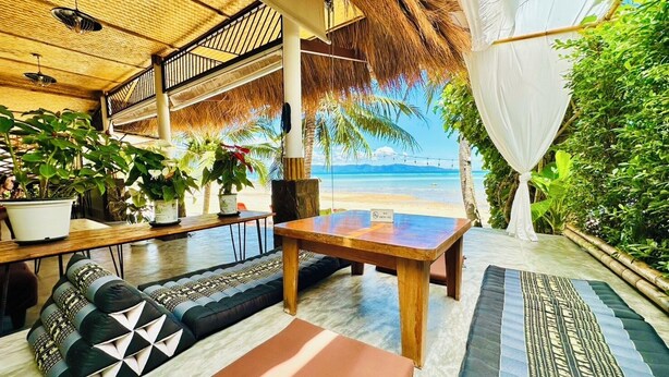 Un área de estar al aire libre con vista a la playa, una mesa de madera y varias plantas en macetas.