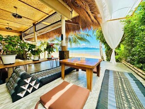 An outdoor seating area with a view of the beach, a wooden table, and several potted plants.