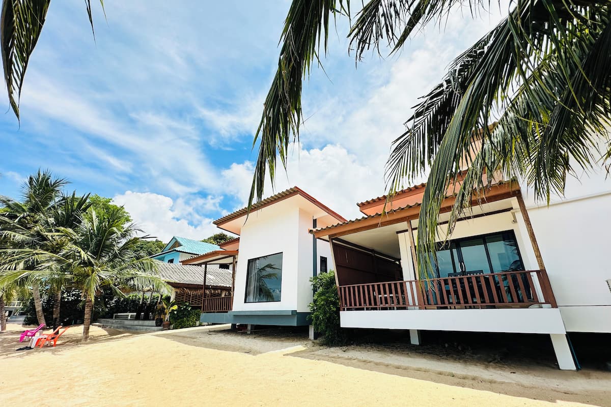 A modern resort with two-story buildings, a sandy beach, and palm trees.