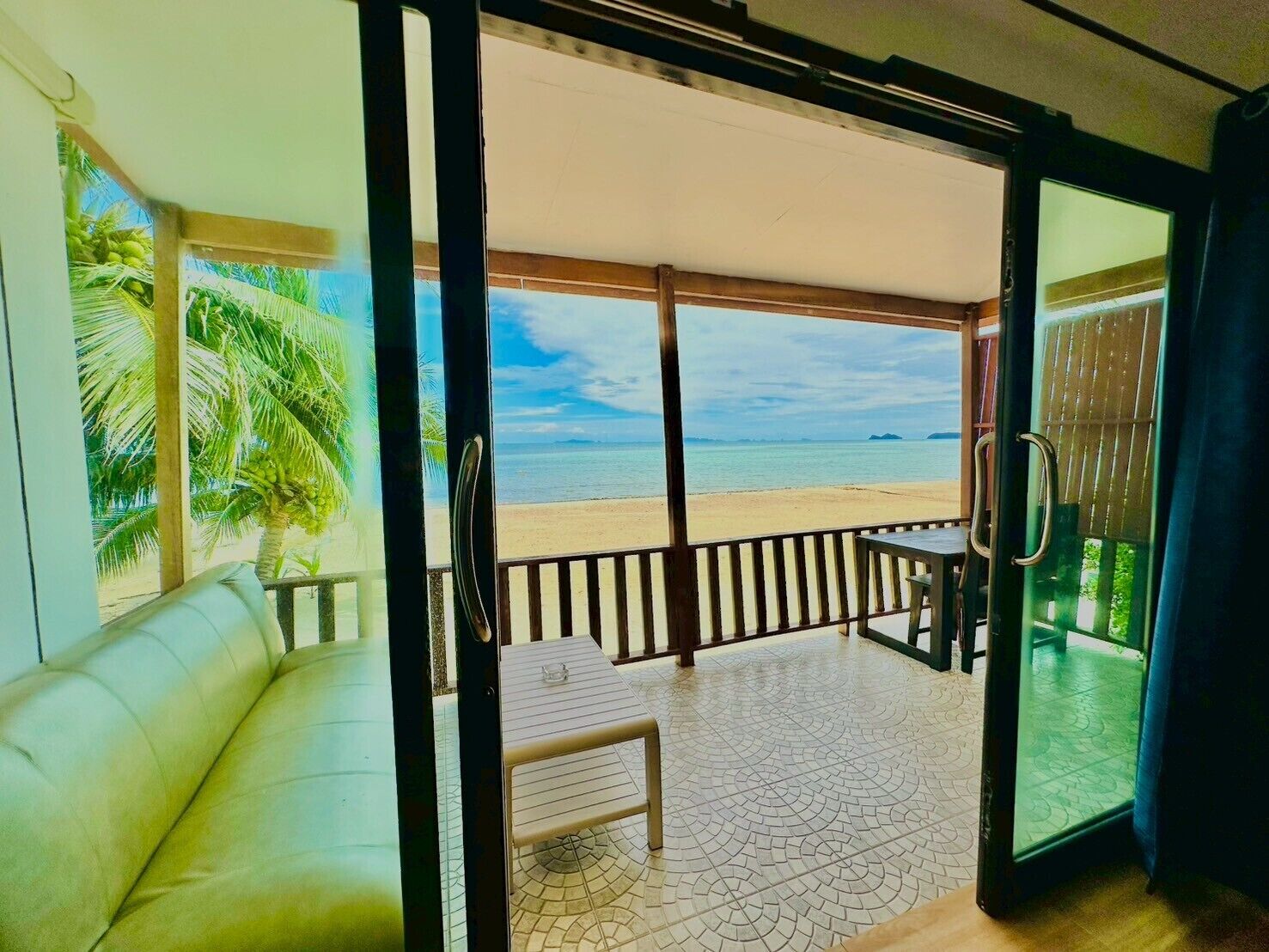 Een kamer met uitzicht op een strand, een bank, een tafel en een glazen deur naar buiten.