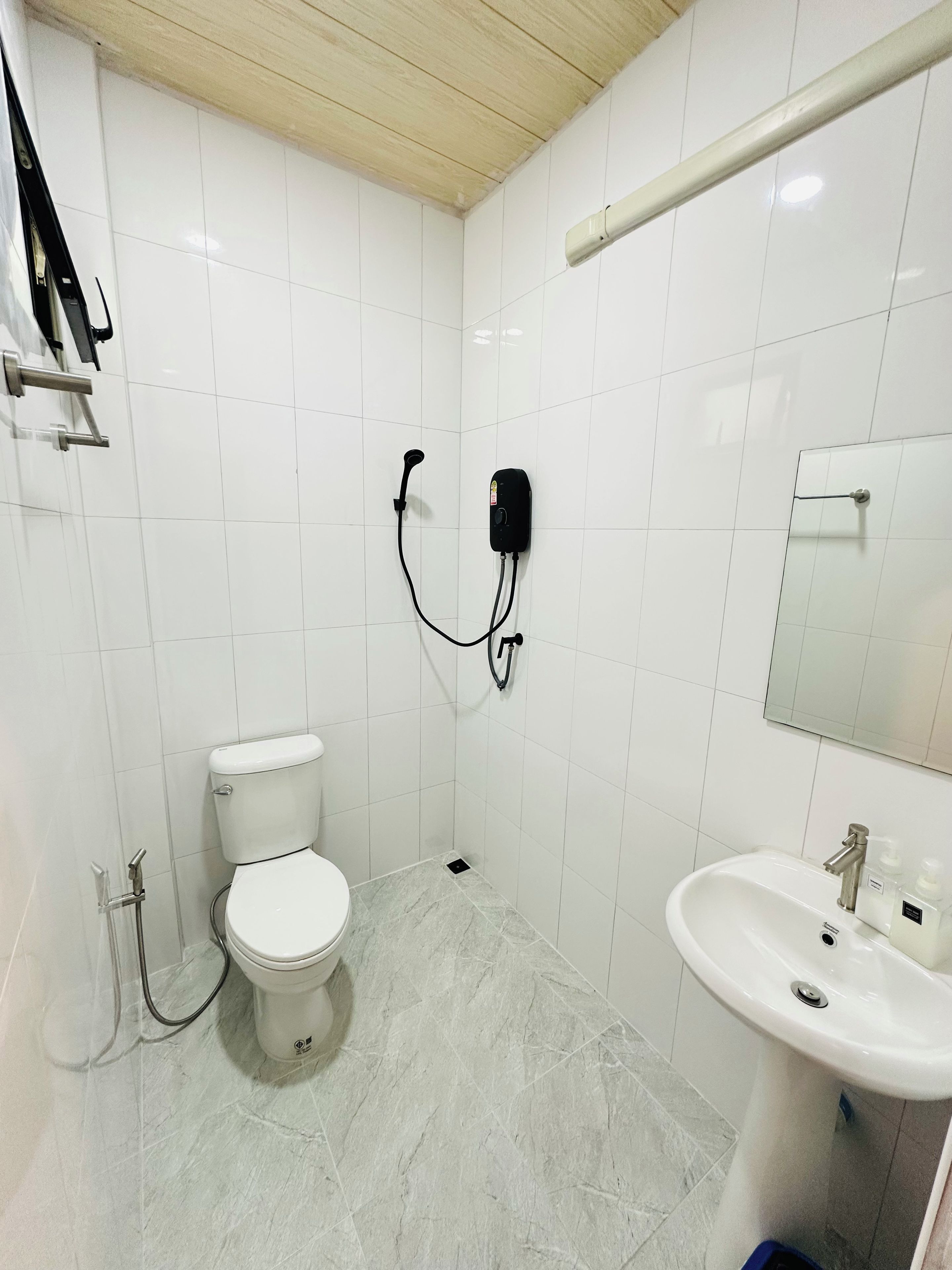 Een badkamer met witte tegels, een toilet, een wastafel en een handdouche.