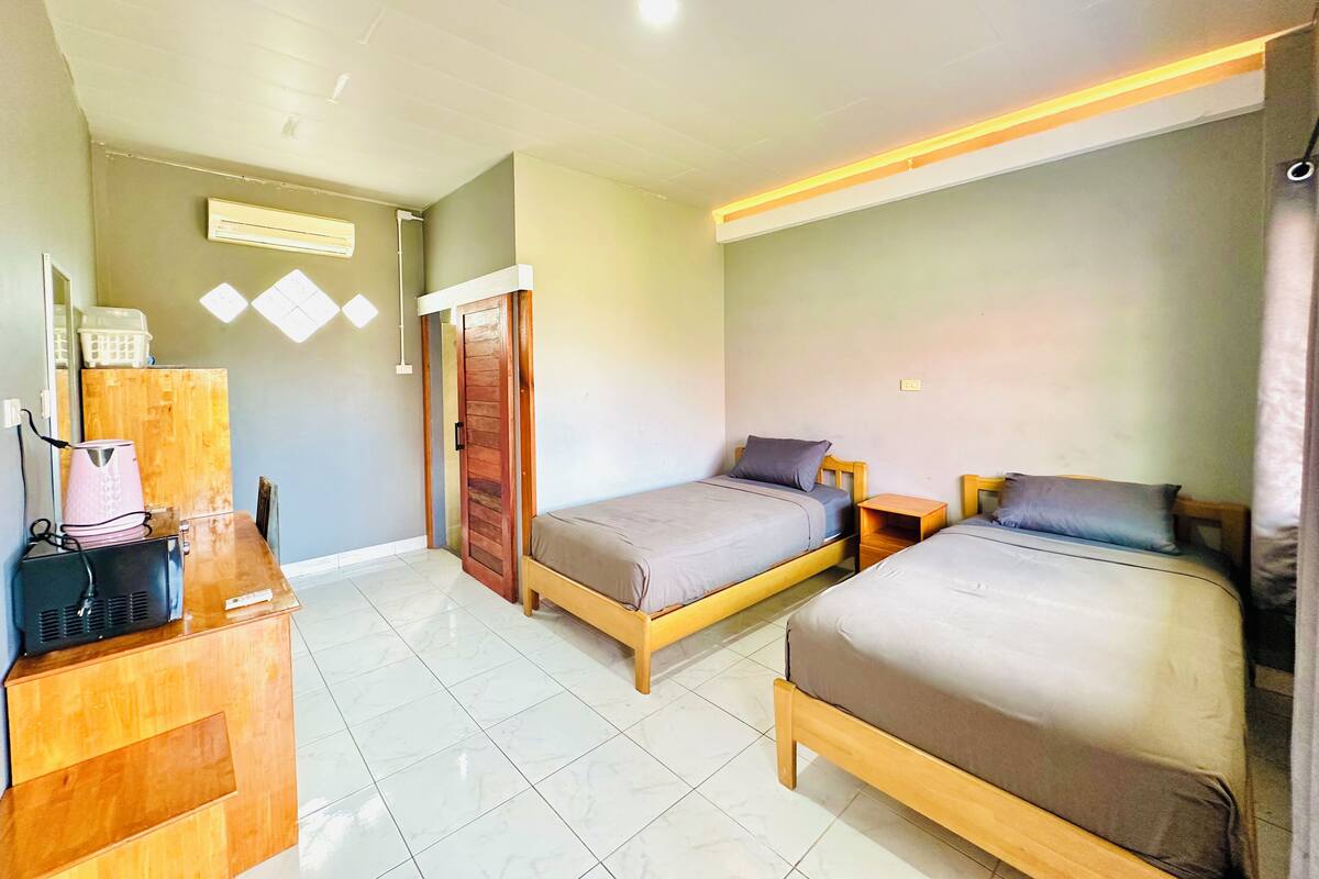 A hotel room with two beds, a wooden desk, a television, and a wardrobe.