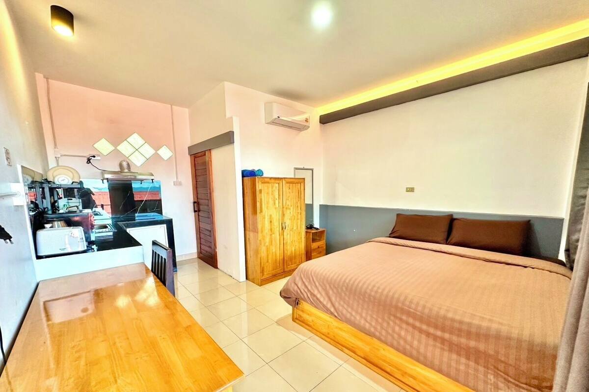 A hotel room with a bed, a wooden desk, a wardrobe, and a kitchenette area.