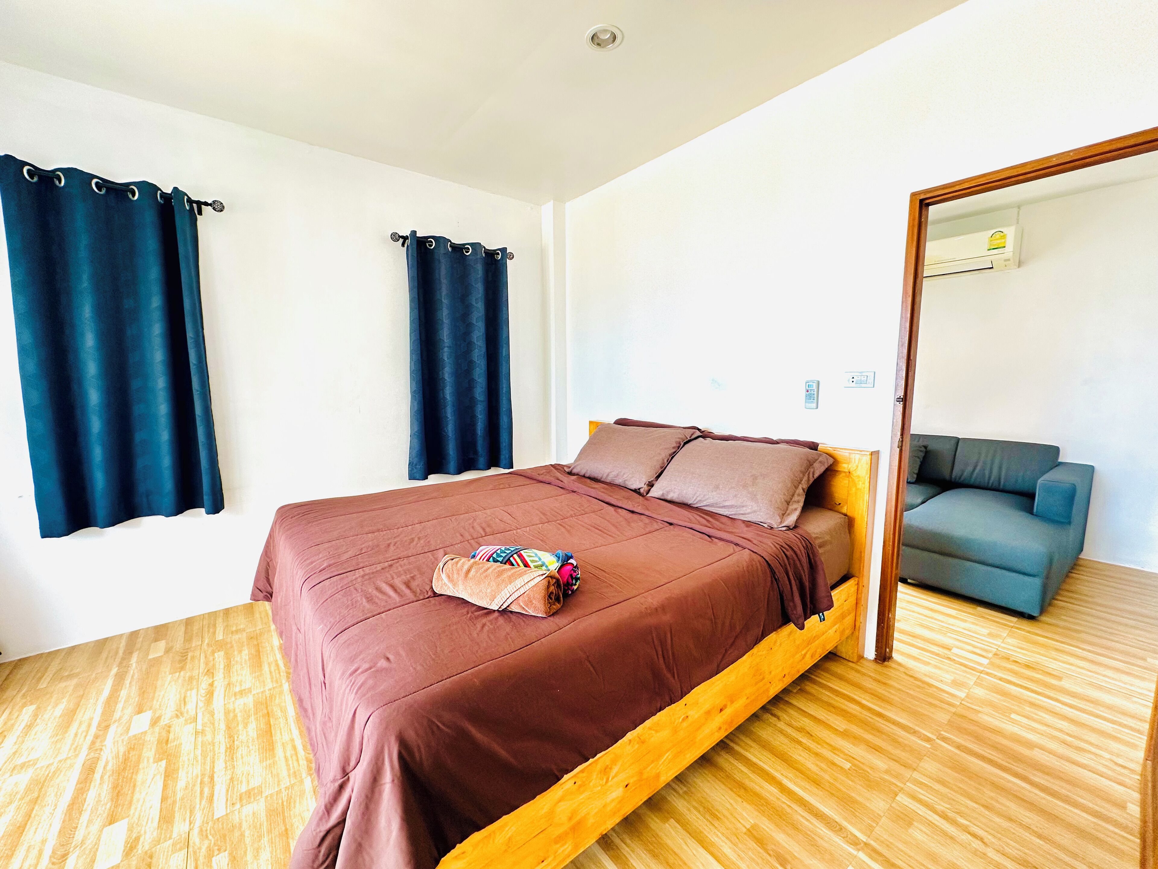 A single bed with a wooden frame and a brown mattress, a blue curtain, and a wooden floor.