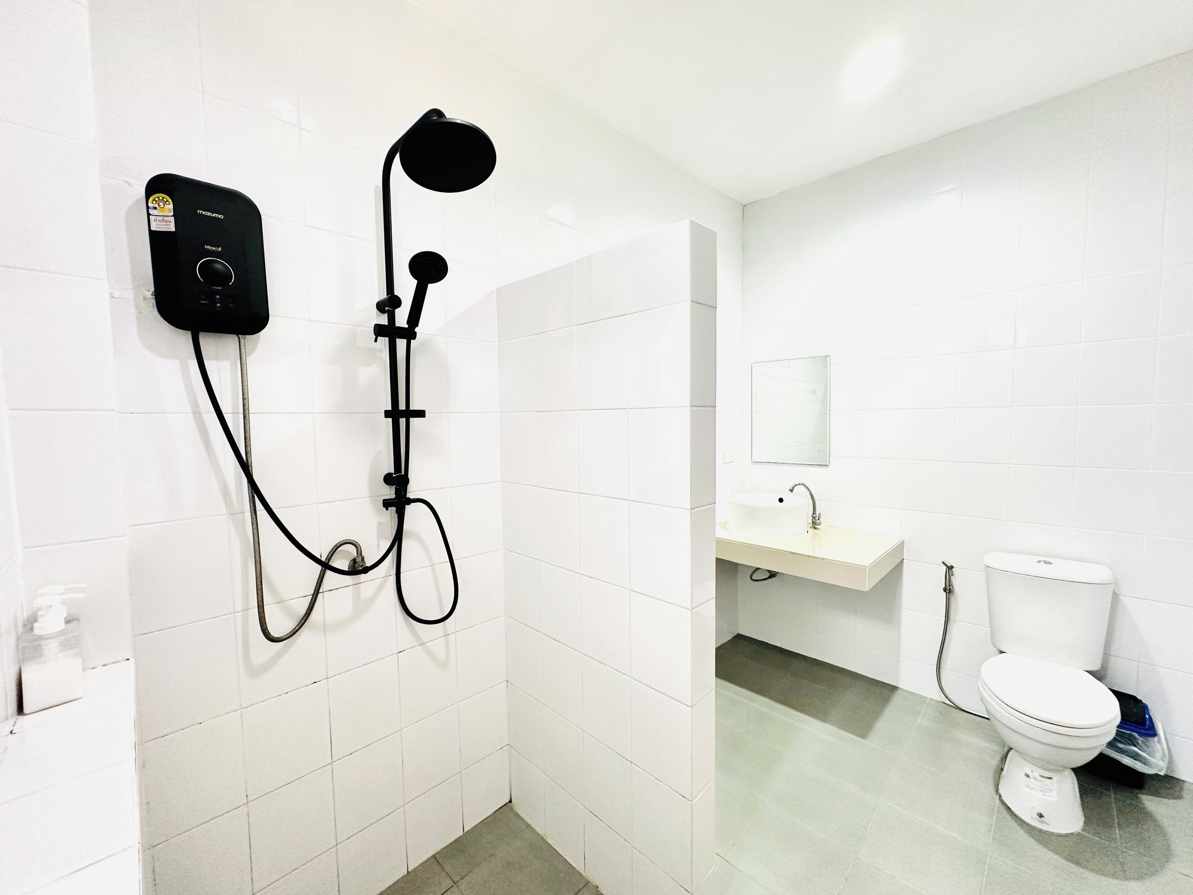 Un baño moderno con un cabezal de ducha manual negro, un panel de control empotrado en la pared, un lavabo blanco con espejo y un inodoro blanco.