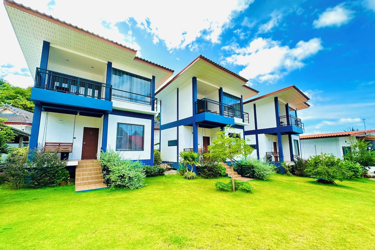 A modern two-story building with balconies, a well-maintained lawn, and a clear blue sky.