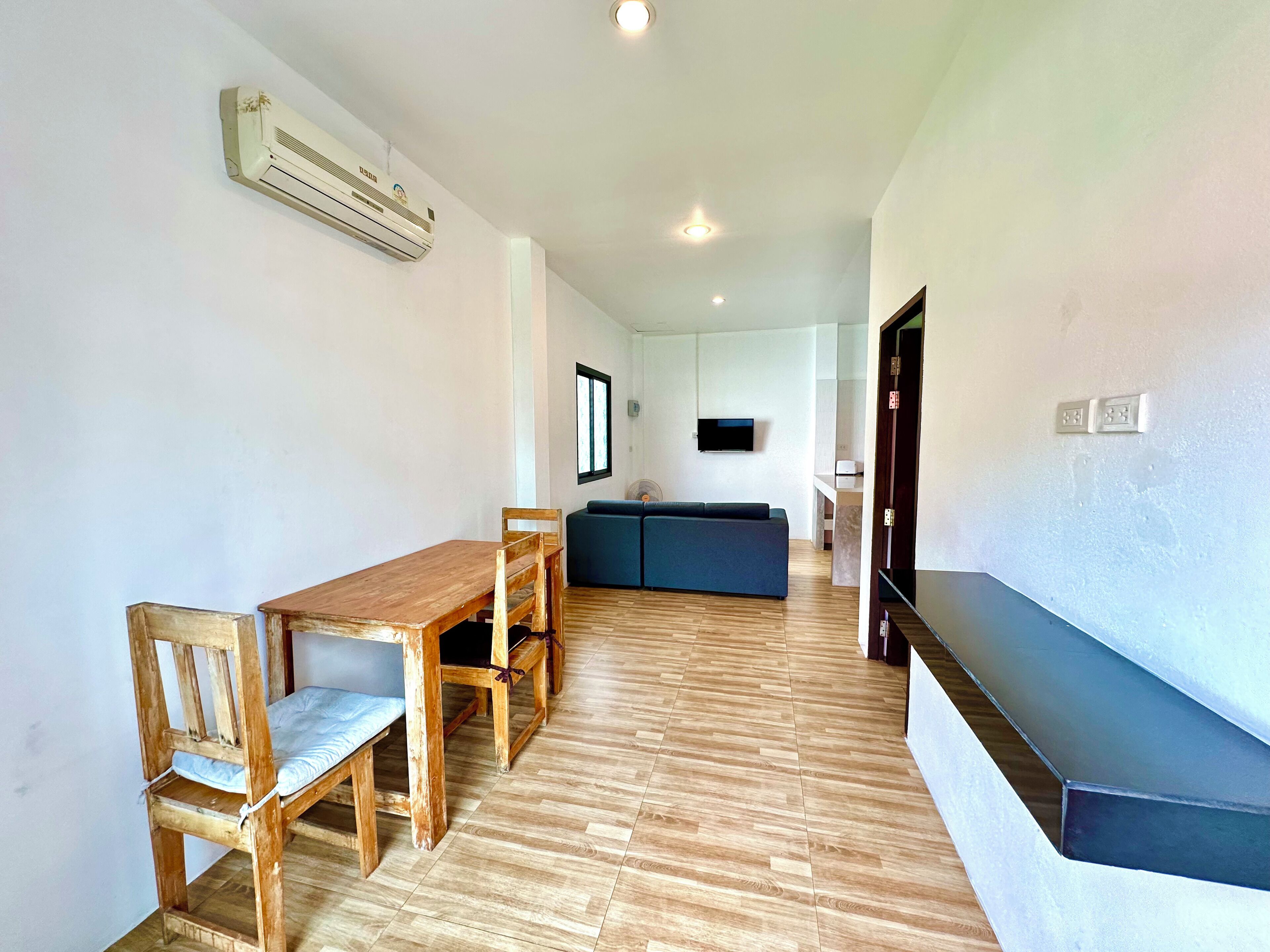 Una habitación con una mesa de comedor y sillas de madera, un sofá azul, un televisor de pantalla plana montado en la pared y un equipo de aire acondicionado.