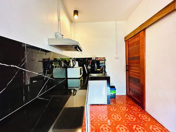 A kitchen with black marble countertops, a white refrigerator, a coffee machine, and a wooden door.