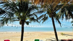 Escena de playa con palmeras, luces colgantes y sillas de plástico de colores.