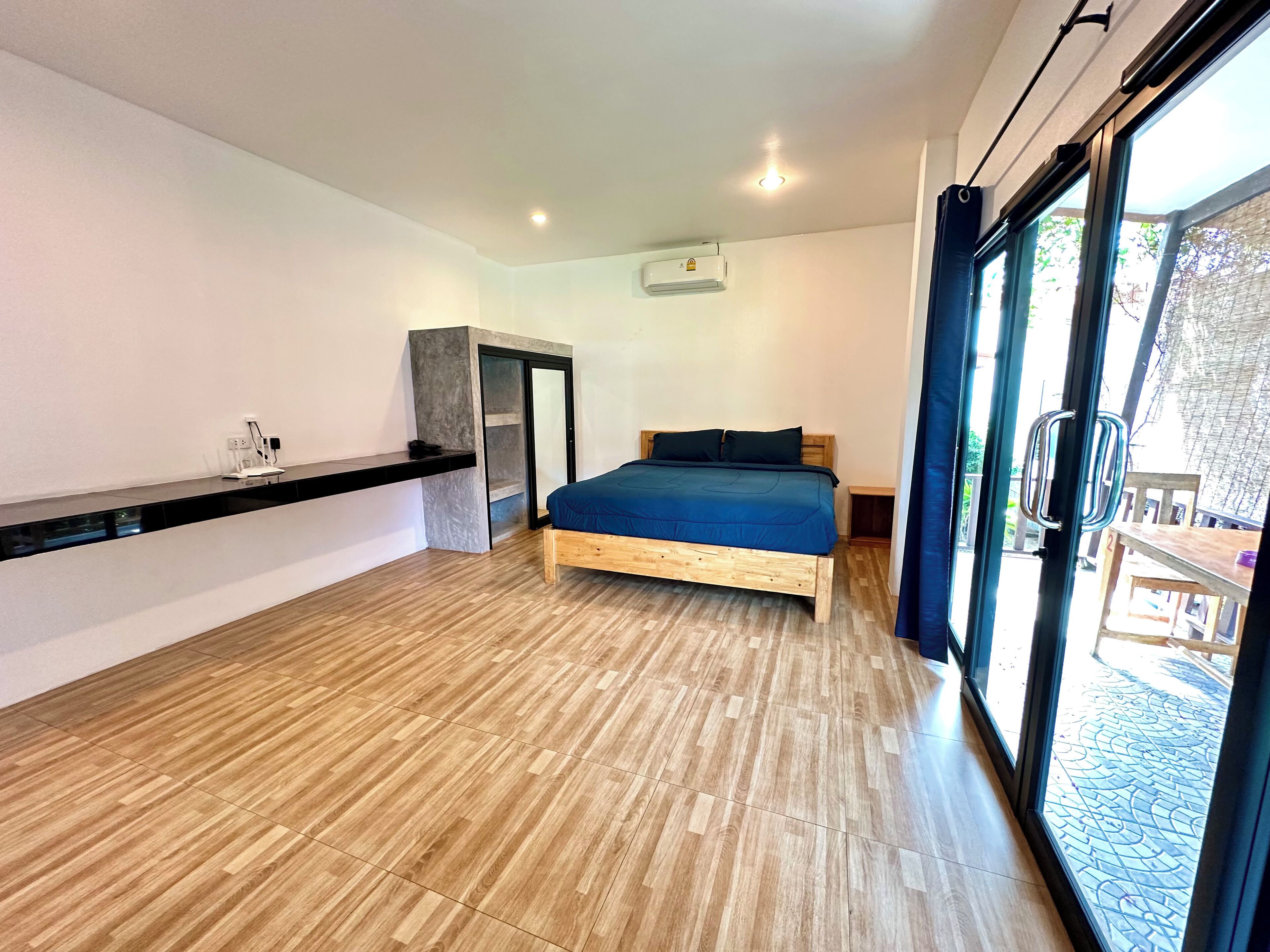 Un dormitorio moderno con una cama de madera, un escritorio empotrado y una puerta corrediza de vidrio que da a un espacio exterior.