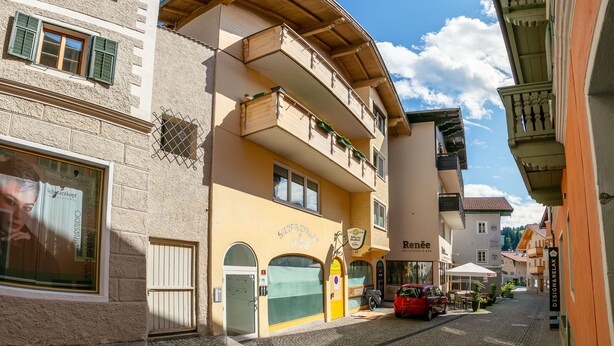 Une rue pavée bordée d’immeubles, dont un restaurant appelé « Renée » et un studio appelé « Schwarzkopf ».