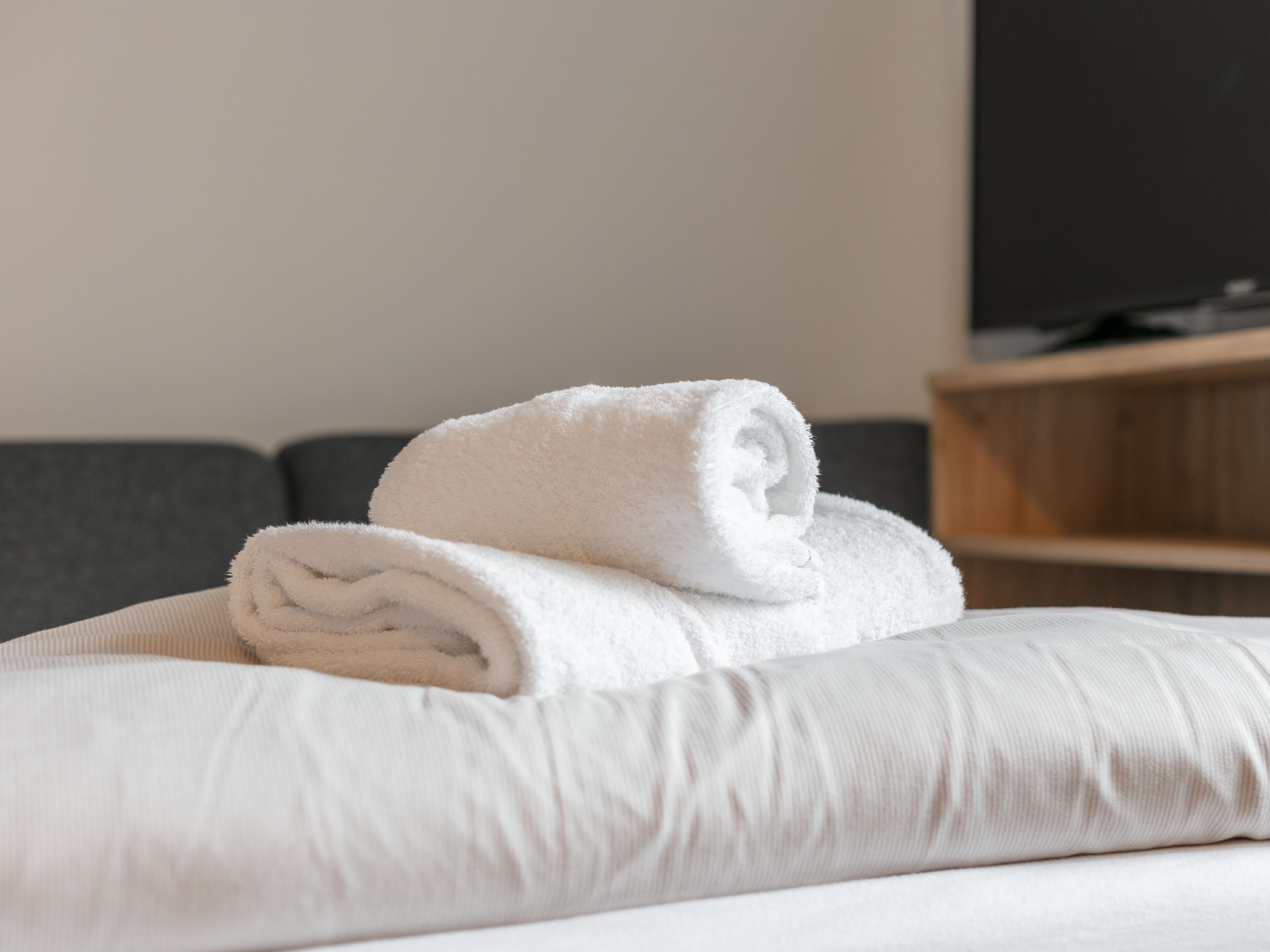 A neatly made bed with a white pillow and a rolled white towel.