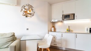 A modern kitchen with white cabinets, a microwave, and a glass dining table. - Golden escape in Funchal (Funchal)