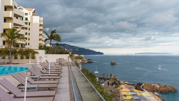 A resort pool area with lounge chairs, a swimming pool, and a view of the sea and distant land. - Golden escape in Funchal (Funchal)