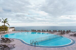 En pool med solstolar, ett palmträd och utsikt över havet.