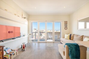 A spacious living room with a large window, a sofa, a TV, and a small table. - GuestReady - Seaview in Costa da Caparica (Almada)