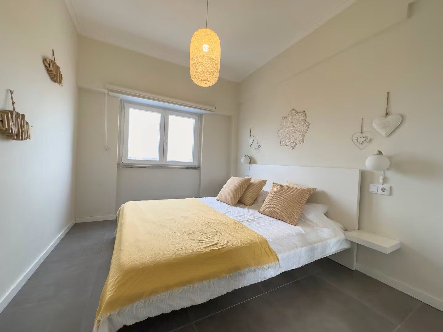 Et soveværelse med en seng, et natbord, en lampe, et vindue og billeder på væggen.