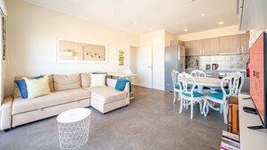 A modern living room with a sofa, a coffee table, and a dining area with chairs. - GuestReady - Seaview in Costa da Caparica (Almada)