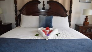 Una cama bien hecha con una colcha azul, almohadas blancas y un arreglo decorativo de flores con forma de corazón sobre la cama.