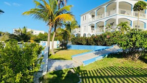 Hotel de dos pisos con fachada blanca y detalles azules, rodeado de abundante vegetación y palmeras.