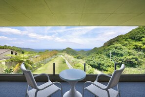 A balcony with a round table and two chairs, overlooking a lush green landscape with hills and a clear sky.