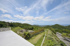 A rooftop terrace with a view of a road and surrounding greenery.
