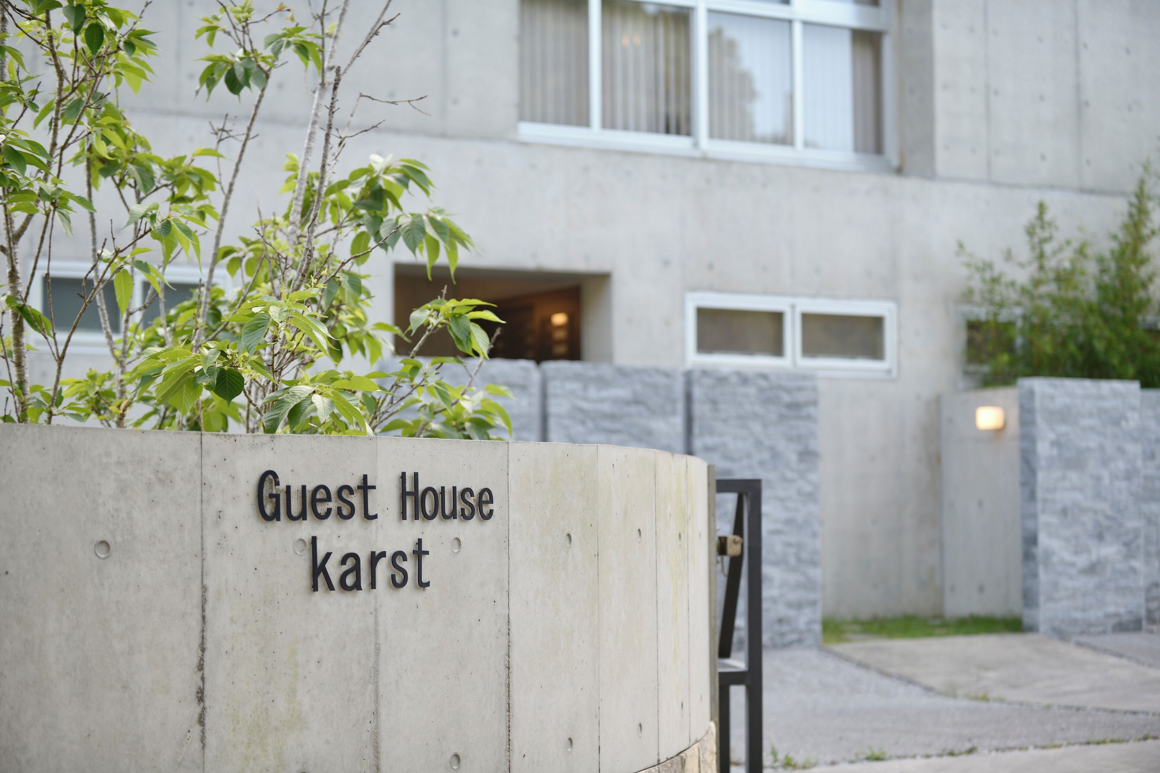 A concrete planter with "Guest House karst" text, a building entrance, and a stone wall.